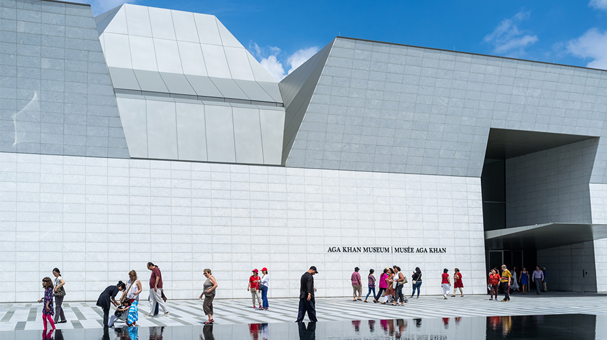 Several people are walking towards to the entrance of a Museum on a bright, sunny day.